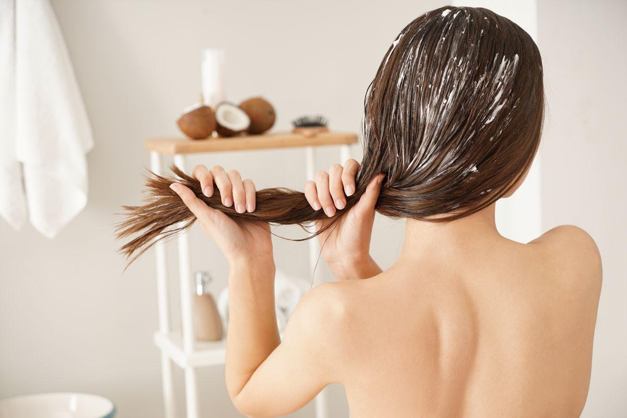 Frau trägt Pflegeprodukt auf langes Haar auf, um Haarbruch zu vermeiden und die Haare mit einem Detangler Spray zu entwirren