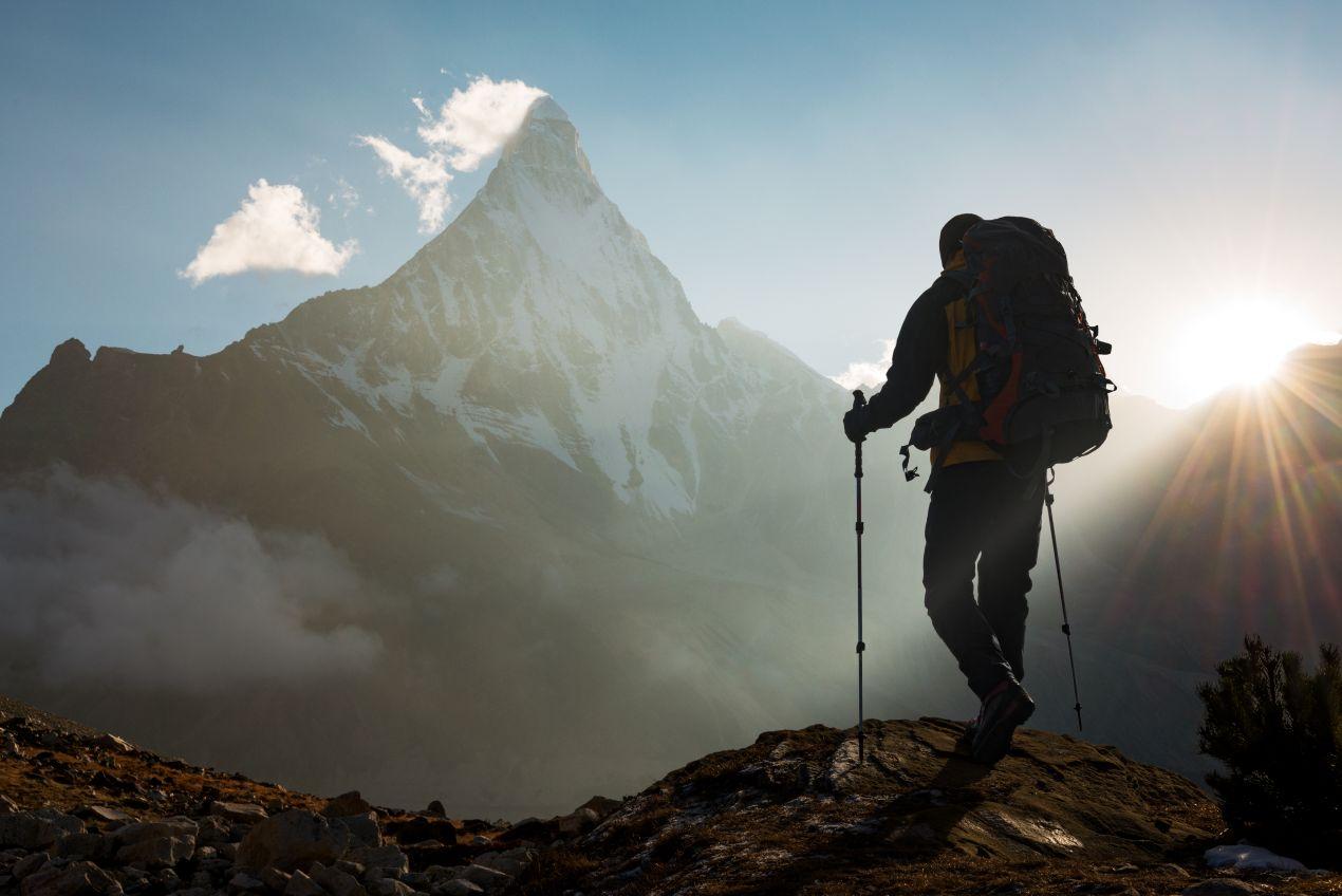 Wanderer mit Rucksack und Wanderstöcken beim Sonnenaufgang, während der Besteigung des Kilimandscharo.