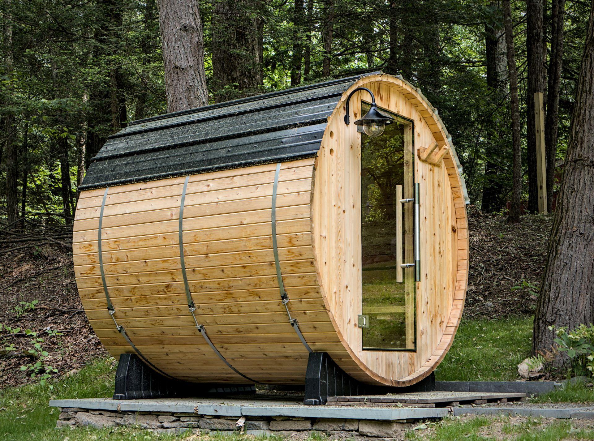 Rustikale Fass-Sauna aus Holz mitten in einer Waldlandschaft.